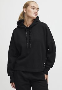 Felpa nera con vestibilità rilassata, caratterizzata da un ampio cappuccio, coulisse e un piccolo logo vicino all'orlo. Tessuto morbido con una superficie liscia.