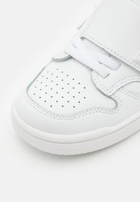 Sneaker bianca in pelle con punta forata, lacci bianchi piatti e colletto imbottito. Presenta un design minimalista e suola in gomma.