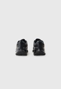 Schwarze GORE-TEX Trailrunningschuhe mit strukturiertem Obermaterial, gepolsterter Kragen und aggressiver Gummisohle für Traktion, ausgelegt für den Einsatz im Freien.