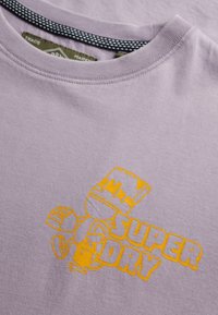 Camiseta de algodón morada con un diseño gráfico que presenta un personaje de dibujos animados y el texto "SUPER DRY" en amarillo brillante, con cuello redondo.