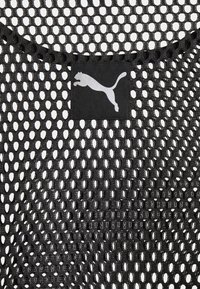 Tissu en mesh noir avec de grands trous ovales et une étiquette carrée noire avec un logo puma blanc centré près de l'encolure.