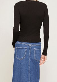 Czarny prążkowany top z długim rękawem w połączeniu z niebieską spódnicą dżinsową z rozporkiem z tyłu i dwiema tylnymi kieszeniami.