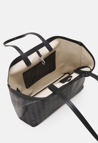 Sac fourre-tout noir à motif avec une surface extérieure lisse et un intérieur beige. Dispose de deux poignées robustes, d'une poche intérieure et d'une fermeture éclair.