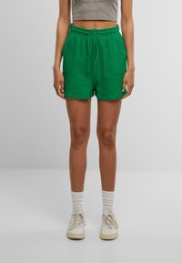 Shorts en coton texturé vert avec une taille élastique et un cordon de serrage. Associés à des baskets beiges et des chaussettes blanches côtelées.