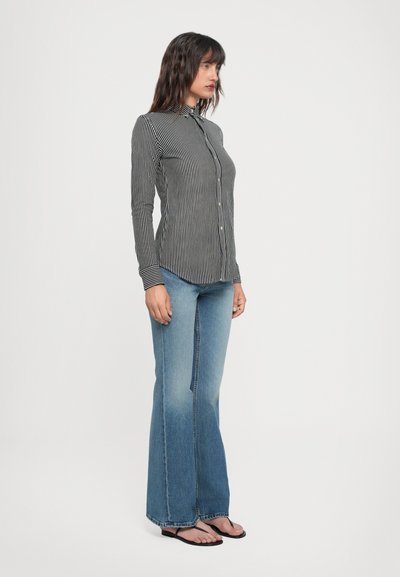 Chemise à boutons noire et blanche à rayures avec un col, associée à un jean évasé bleu clair et des tongs noires.