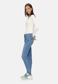 Jasnoniebieskie slim-fit dżinsy z klasycznym pięciopocketowym wzorem, w połączeniu z dopasowanym białym longsleeve'm i trampkami z zielonymi akcentami.