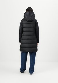 Zwarte pufferjas met capuchon, voorzien van een gevoerd ontwerp en een iets langere pasvorm, gecombineerd met wijde denim broek.