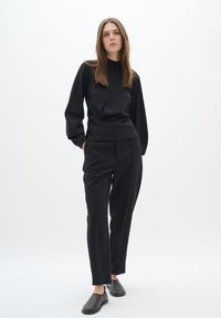 Black long-sleeve top with a round neckline, paired with high-waisted, tailored black pants and black slip-on shoes. Smooth fabric, fitted design.