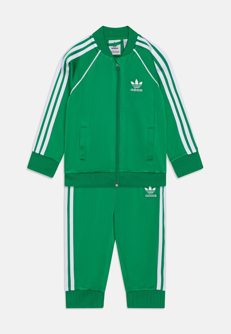 Fato de treino verde da Adidas com detalhes em brancos nas três riscas. A jaqueta possui fecho de correr e punhos canelados, enquanto as calças têm punhos elásticos.