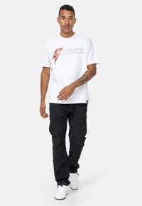 Hvid bomulds t-shirt med David Bowie grafisk logo, afslappet pasform. Blandet med sorte cargo bukser og hvide sneakers for et afslappet look.