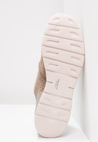 Beige perforerad lädersko med vadderad krage och sula i vitt gummi med strukturerade spår för grepp.