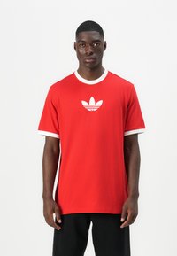 Κόκκινο βαμβακερό t-shirt με λευκό γιακά και μανίκια, με λευκό λογότυπο Adidas στο κέντρο του στήθους. Κοντά μανίκια και χαλαρή εφαρμογή.