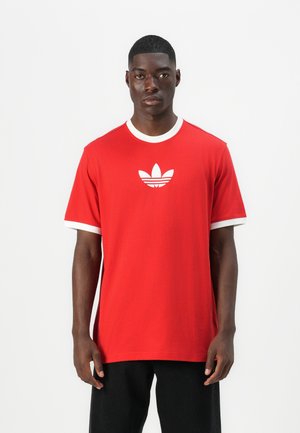 Camiseta de algodón roja con cuello y puños en blanco, con un logotipo de Adidas blanco centrado en el pecho. Manga corta y corte relajado.