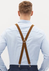 Brune stofsuspendere med metalclips, båret over en lyseblå skjorte, krydser bagpå med en trekantet forbindelse.