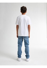 Camiseta blanca de manga corta con un corte relajado, combinada con jeans de mezclilla azul claro y zapatillas blancas. Costuras visibles en los jeans.