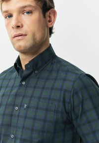 Camicia a quadri verde e blu navy con colletto, chiusura con bottoni, taschino sul petto e tessuto texturizzato.