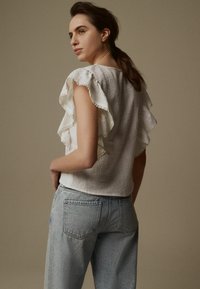 Haut blanc à manches courtes avec des accents volantés et de la dentelle, associé à un jean en denim léger taille haute bleu clair. Texture douce et coupe décontractée.