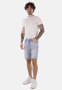 Shorts in denim azzurro chiaro con orlo sfilacciato, dotati di tasche frontali e dettagli leggermente strappati. Abbinati a una t-shirt aderente bianca e a sneakers bianche.