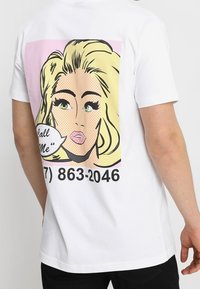 Blonde vrouw met groene ogen in popart-stijl op een witte blouse, spraakballon zegt "Bel me," telefoonnummer eronder.