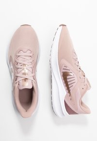Chaussures de sport rose clair avec tige en mesh, semelle blanche et accents en or rose. Bout arrondi et intérieur rembourré pour le confort.