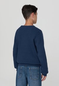 Granatowy sweter o teksturze, z okrągłym dekoltem i długimi rękawami, w zestawie z jasnoniebieskimi dżinsami z tylnymi kieszeniami.