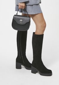 Czarne kozaki do kolan na grubym obcasie, wykonane z zamszu z gładką boczną panelem i detalem zamka. W zestawie z fakturowaną czarną torebką.