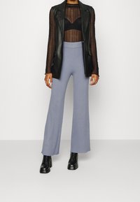 Svart läder utan ärmar blazer över en genomskinlig svart långärmad topp, parat med ljusblå ribbade utsvängda byxor och svarta ankelstövlar.