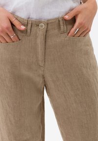 Ljusbruna linbyxor med avslappnad passform, med knappställning, bältesloopar och sidofickor. Diskret struktur synlig.