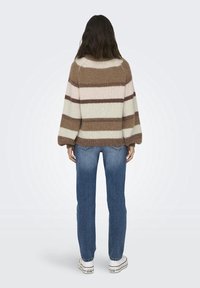 Sweter w paski z długimi, dzwonowymi rękawami. Kolory to jasnoróżowy, beżowy i kremowy. Zestawiony z niebieskimi dżinsami i białymi trampkami.