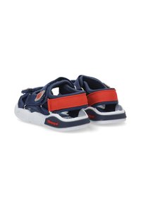 Sandalias azul marino con correas rojas, hechas de tela y goma. Diseño abierto con cierres ajustables y suelas texturizadas blancas.