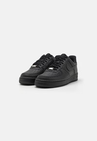 Black low-top sneakers with textured leather, perforated design, flat laces, and rubber soles. Features subtle branding on the side.