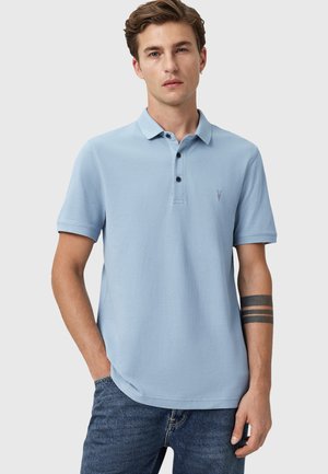 Lyseblå polo skjorte med klassisk krave, to-knappers stolpe og korte ærmer. Har et lille broderet logo på brystet.