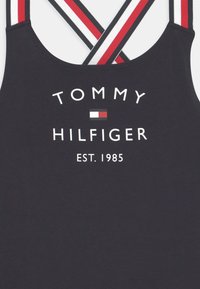Czarny top na ramiączkach z popsutymi czerwonymi, białymi i czarnymi paskami, napis "Tommy Hilfiger", logo oraz nadruk "EST. 1985" z przodu.