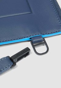 Marineblauwe leren accessoire met een gestructureerde afwerking, voorzien van een zwart metalen clip en een contrasterende blauwe voering langs de rits.