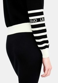 Maglione a righe in bianco e nero con dettaglio del logo sulla manica, polsini a costine e piccole perle lungo la riga.
