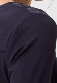 Marineblaue, kurzärmlige Bluse mit glatter Textur und einem kontrastierenden dunklen Einsatz an den Schultern sowie einem einfachen, minimalistischen Design.
