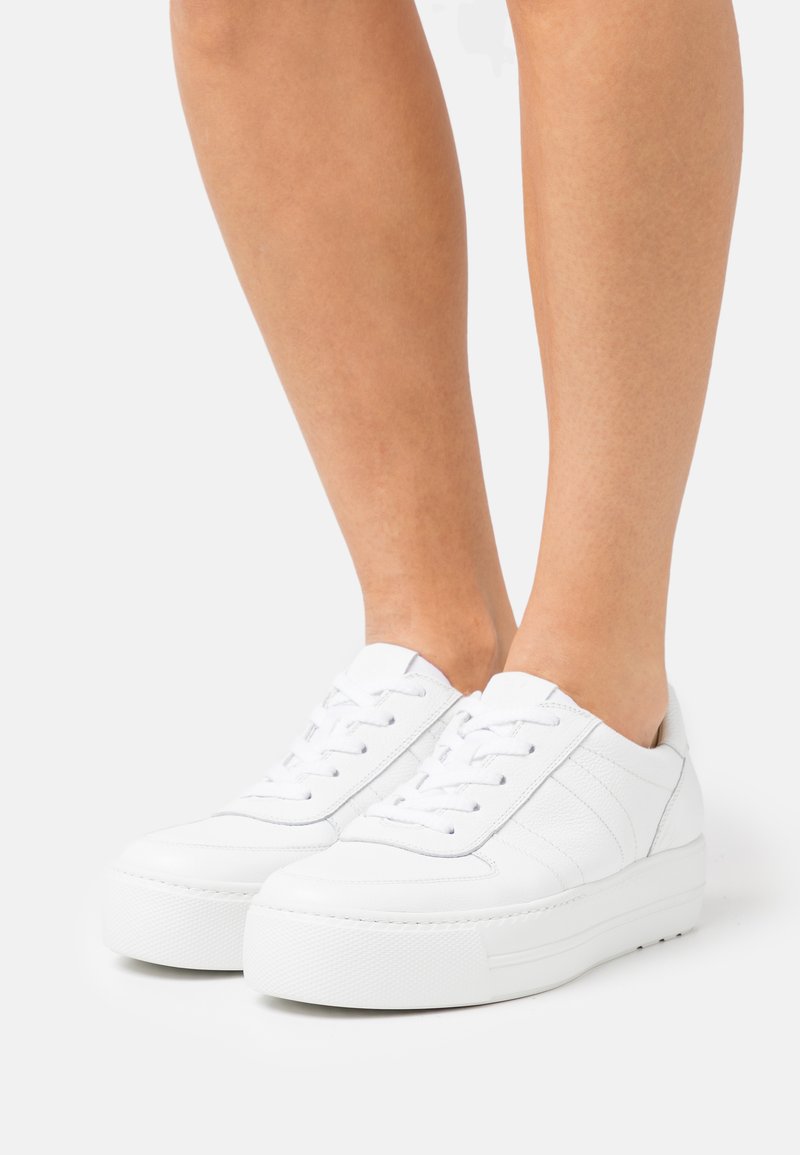 Baskets en cuir blanc avec un design texturé, dotées d'une semelle épaisse et de lacets contrastés. Style minimaliste avec des accents subtils.