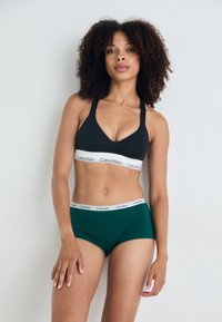 Black sports bra with a white Calvin Klein logo band and green boyshorts with a matching logo band, both made of smooth fabric.