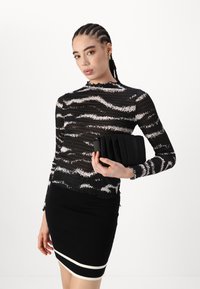Fekete-fehér csíkos hosszúujjú felső textúrált anyagból, fekete, testhez álló szoknyával és redős fekete clutch táskával párosítva.
