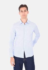 Camicia a righe blu chiaro con colletto button-down, maniche lunghe e vestibilità slim; abbinata a jeans blu scuro con taglio dritto.