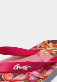 Ροζ σαγιονάρα με σόλα σε σχέδιο λουλουδιών και φωτεινά κόκκινους ιμάντες που φέρουν λευκό λογότυπο "Guess" στο πλευρικό ιμάντα.