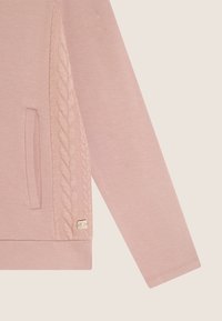 Felpa rosa chiaro con un pannello in maglia a treccia testurizzata di lato, caratterizzata da un piccolo logo metallico e una tasca frontale.