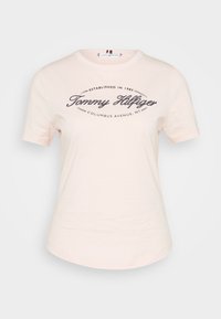 Světle růžové bavlněné tričko s kulatým výstřihem. Na přední straně je tmavě modrý potištěný logo s nápisem "Tommy Hilfiger" a údaji o místě.