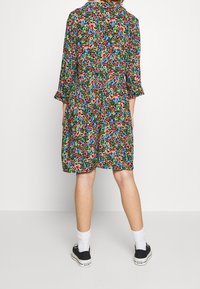 Blommig klänning med en grön bakgrund och röda, blå och rosa blommor. Trekvartsärmar och en avslappnad passform. Kombineras med svarta sneakers.