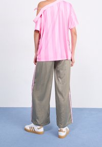 Rosa randig oversized topp med en axel bar, tillsammans med grå ränder vid vida byxor och vita sneakers med bruna detaljer.