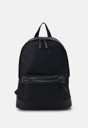 Czarny plecak z gładką tkaniną na zewnątrz, zaokrąglonym kształtem, podwójnym zamkiem błyskawicznym, przednią kieszenią i minimalistycznym wzornictwem.
