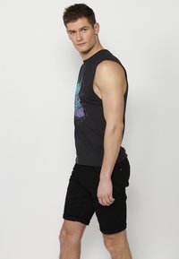 Svart ärmlös tröja med färggrafisk design, kombinerad med svarta uppvikta shorts. Tyget verkar slätt, med en åtsittande form.