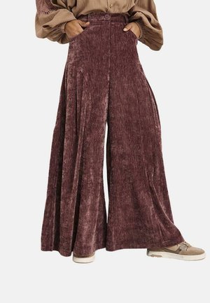 Pantalones de terciopelo marrón de pierna ancha y cintura alta, combinados con zapatillas beige y una blusa beige de manga larga con mangas abullonadas y detalles de encaje.