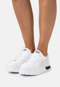 White platform sneakers with lace-up design, featuring a smooth leather texture, branded accents, and contrasting sole details.