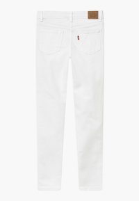 Vaqueros skinny de mezclilla blanca con una textura suave, cinco bolsillos y una etiqueta de piel marrón en la cintura. Incluye una pequeña etiqueta de logo roja en el bolsillo trasero.